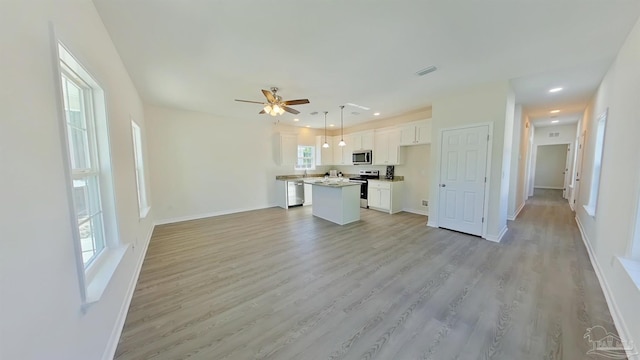 kitchen with a wealth of natural light, white cabinetry, a center island, decorative light fixtures, and appliances with stainless steel finishes