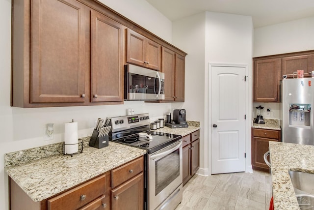 kitchen with appliances with stainless steel finishes, brown cabinetry, and light stone countertops