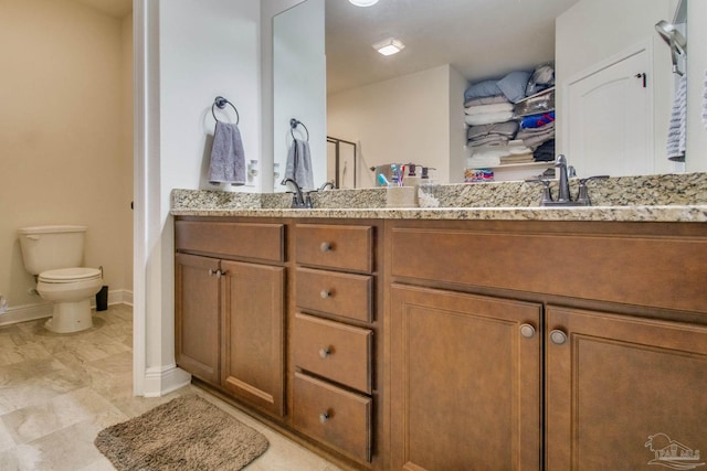 full bath featuring double vanity, a sink, toilet, and baseboards