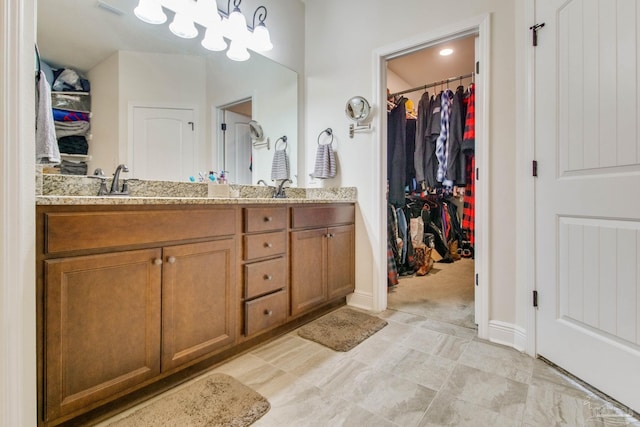 full bath featuring double vanity, baseboards, a walk in closet, and a sink