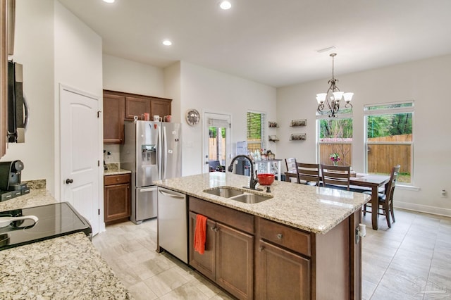 kitchen featuring a sink, appliances with stainless steel finishes, light stone countertops, an island with sink, and decorative light fixtures