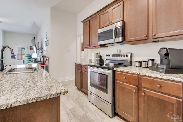 kitchen with baseboards, brown cabinetry, appliances with stainless steel finishes, light stone counters, and a sink