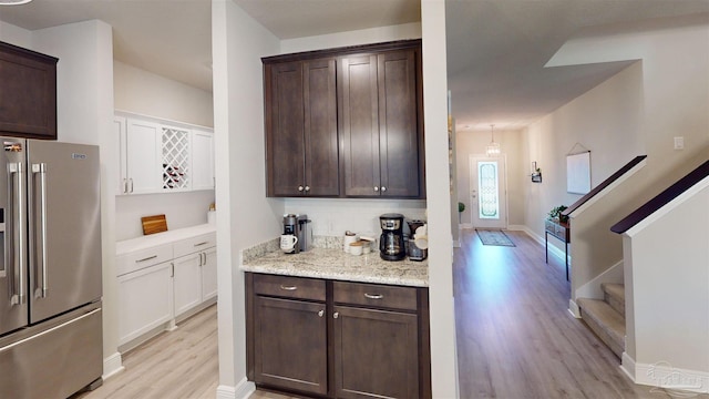 kitchen with tasteful backsplash, high quality fridge, dark brown cabinetry, light wood-type flooring, and light stone counters