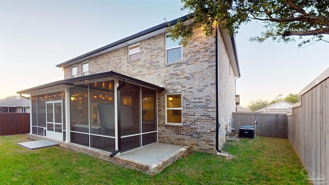 back house at dusk featuring a lawn, cooling unit, and a sunroom