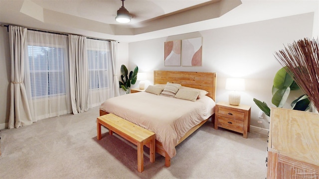 carpeted bedroom with ceiling fan and a tray ceiling