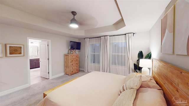 bedroom with ensuite bath, light colored carpet, ceiling fan, and a tray ceiling