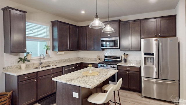 kitchen featuring pendant lighting, appliances with stainless steel finishes, dark brown cabinetry, a kitchen island, and sink