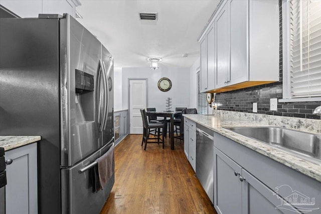 kitchen with light stone countertops, tasteful backsplash, stainless steel appliances, gray cabinets, and dark hardwood / wood-style floors