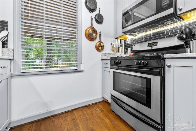 kitchen with light stone countertops, tasteful backsplash, stainless steel appliances, dark hardwood / wood-style floors, and white cabinetry