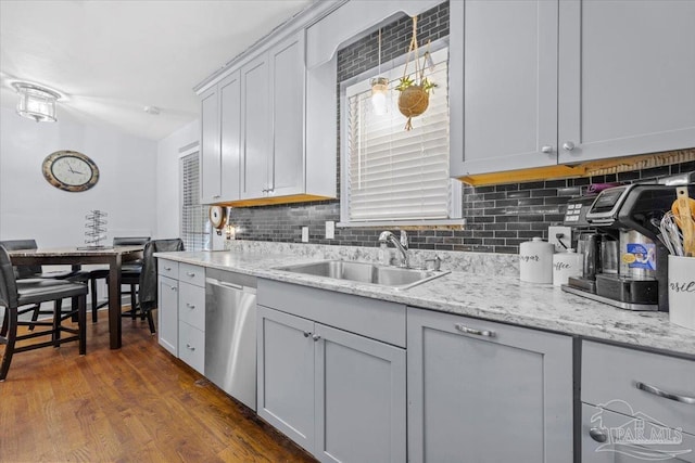 kitchen with backsplash, light stone counters, stainless steel dishwasher, sink, and dark hardwood / wood-style floors