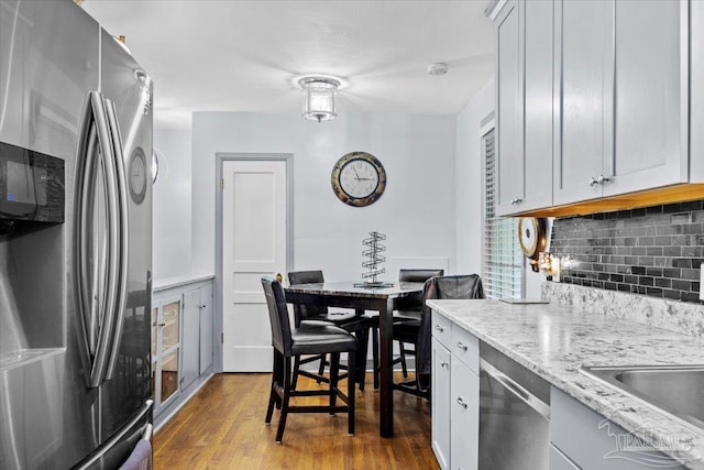 kitchen with backsplash, light stone counters, stainless steel appliances, light hardwood / wood-style flooring, and white cabinets