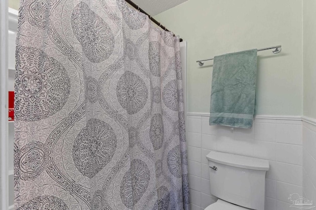 full bath with toilet, tile walls, a shower with shower curtain, and a wainscoted wall