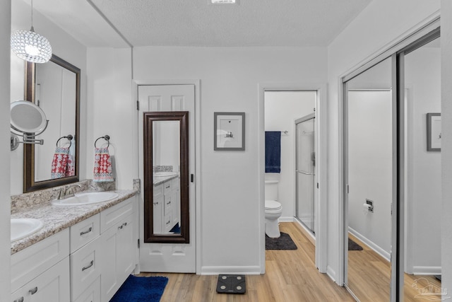 full bath with a sink, toilet, double vanity, a shower stall, and wood finished floors