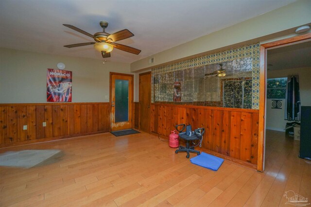 misc room featuring ceiling fan, light hardwood / wood-style floors, and wooden walls