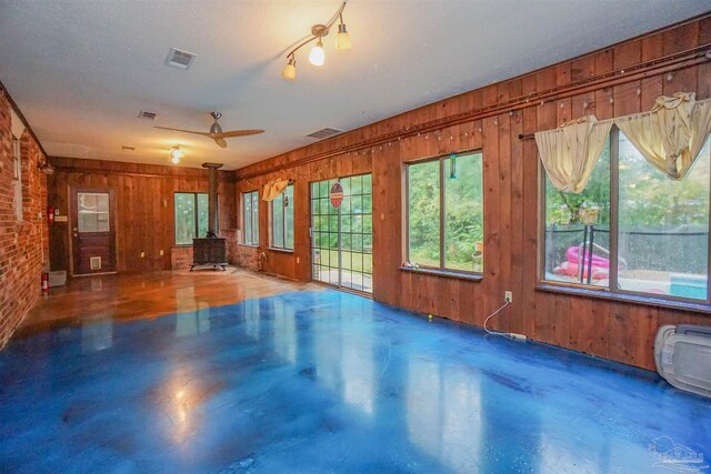 unfurnished living room with a textured ceiling, a wood stove, ceiling fan, and wooden walls