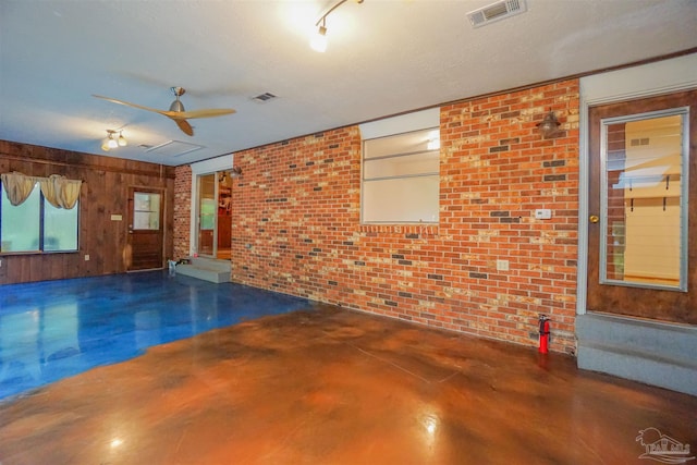 empty room with wooden walls, ceiling fan, a textured ceiling, and brick wall