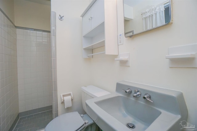 bathroom featuring tiled shower, toilet, and sink