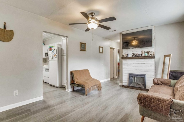 living room featuring ceiling fan, light hardwood / wood-style flooring, and a fireplace