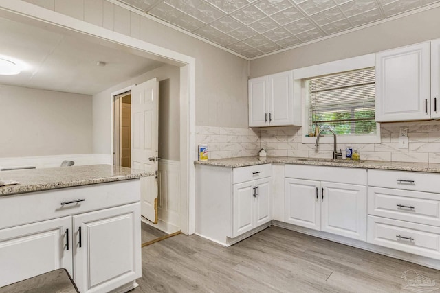 kitchen with light hardwood / wood-style flooring, light stone counters, sink, and white cabinets