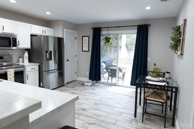 kitchen with appliances with stainless steel finishes, light hardwood / wood-style flooring, white cabinets, and tasteful backsplash