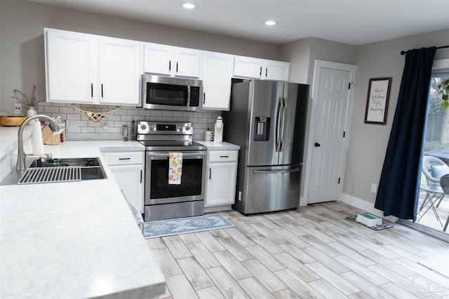 kitchen featuring light hardwood / wood-style flooring, backsplash, white cabinetry, appliances with stainless steel finishes, and sink