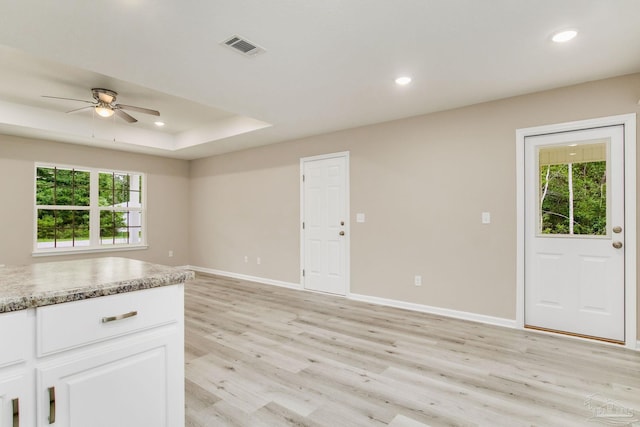 kitchen featuring light stone counters, a raised ceiling, ceiling fan, light hardwood / wood-style floors, and white cabinetry