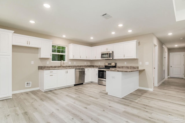 kitchen featuring sink, stainless steel appliances, dark stone counters, white cabinets, and light wood-type flooring