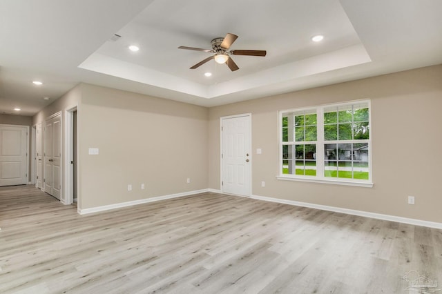 unfurnished room featuring ceiling fan, a tray ceiling, and light hardwood / wood-style flooring