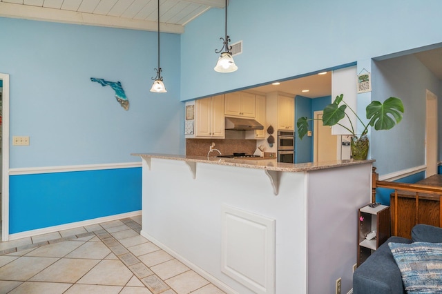 kitchen with under cabinet range hood, a breakfast bar, light tile patterned floors, tasteful backsplash, and hanging light fixtures