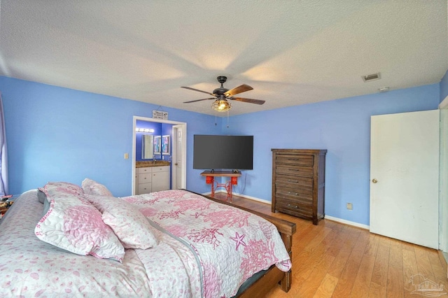 bedroom featuring baseboards, wood finished floors, visible vents, and a textured ceiling