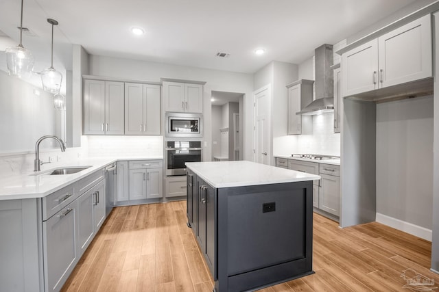 kitchen featuring light wood-type flooring, gray cabinetry, a sink, stainless steel appliances, and wall chimney exhaust hood