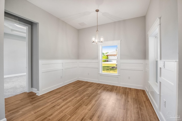 spare room featuring a decorative wall, a notable chandelier, wainscoting, and light wood finished floors