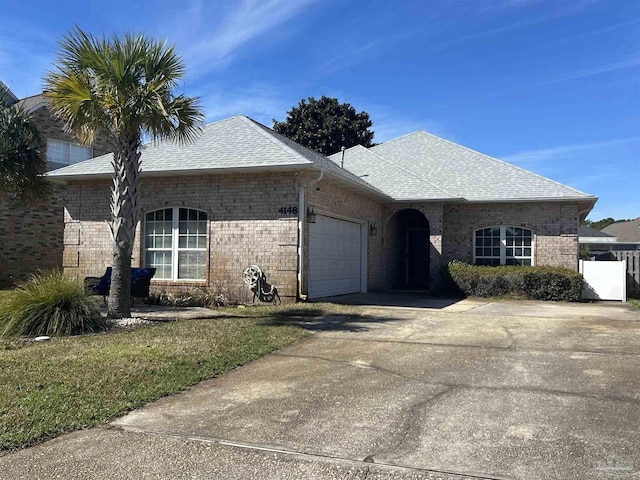 single story home featuring a shingled roof, brick siding, driveway, and an attached garage