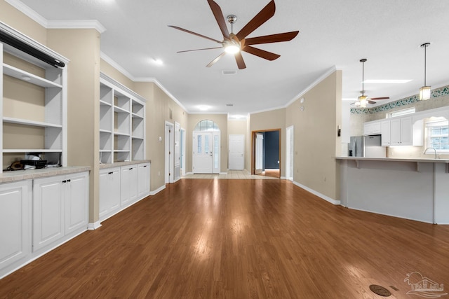 unfurnished living room featuring a ceiling fan, ornamental molding, a sink, wood finished floors, and baseboards