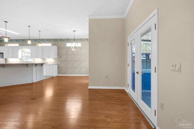 unfurnished living room featuring french doors, crown molding, baseboards, and wood finished floors