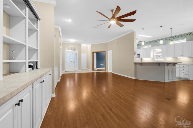 unfurnished living room with crown molding, baseboards, ceiling fan, and wood finished floors