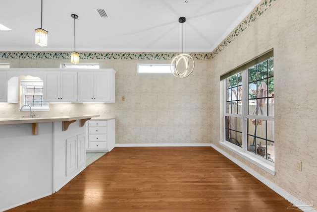 unfurnished dining area featuring visible vents, a sink, baseboards, and wood finished floors