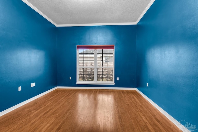 empty room with crown molding, a textured ceiling, baseboards, and wood finished floors