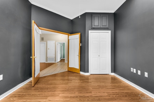 unfurnished bedroom featuring light wood-style flooring, visible vents, baseboards, a closet, and crown molding