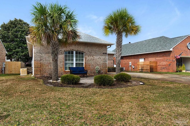 back of house featuring driveway, a yard, central air condition unit, and brick siding