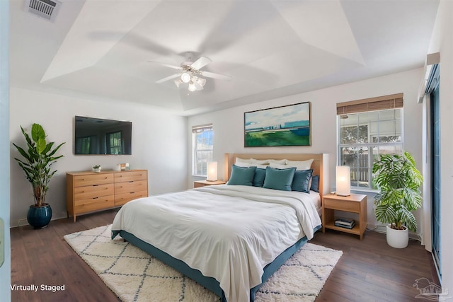 bedroom featuring a ceiling fan, visible vents, a tray ceiling, and wood finished floors