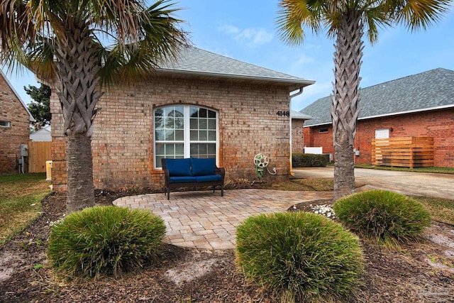 rear view of house with brick siding, roof with shingles, a patio area, and fence