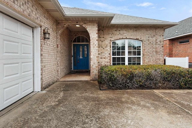 doorway to property with a garage, roof with shingles, and brick siding