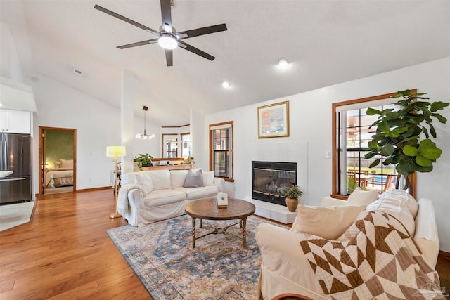 living room with ceiling fan with notable chandelier, light hardwood / wood-style floors, and high vaulted ceiling