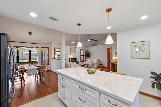 kitchen featuring stainless steel fridge, light hardwood / wood-style floors, a kitchen island, ceiling fan, and decorative light fixtures