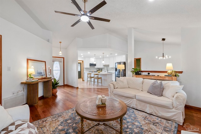 living room with a textured ceiling, ceiling fan with notable chandelier, dark hardwood / wood-style floors, and high vaulted ceiling