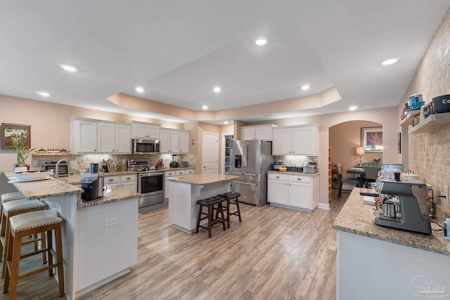 3246 Main St, Navarre, FL 32566 - kitchen with arched walkways, light wood-style flooring, a breakfast bar area, a tray ceiling, and stainless steel appliances