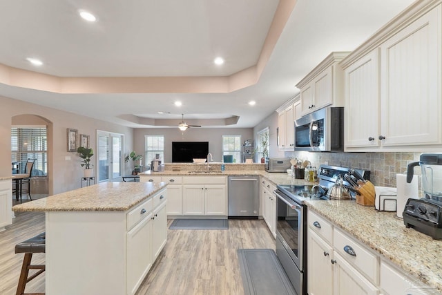 3246 Main St, Navarre, FL 32566 - kitchen with light wood-style flooring, a peninsula, a sink, appliances with stainless steel finishes, and a raised ceiling