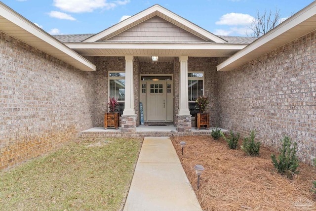 view of exterior entry with roof with shingles, a porch, and brick siding