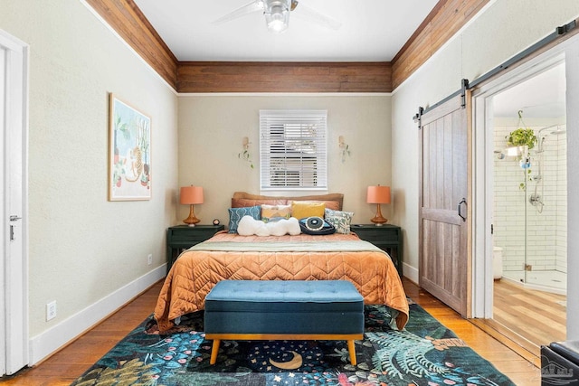 bedroom featuring ceiling fan, baseboards, light wood-type flooring, a barn door, and ensuite bathroom